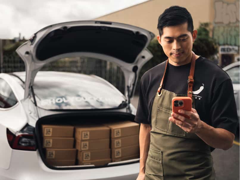 Quickbooks online customer looking at their mobile phone in front of a car loaded with supplies.