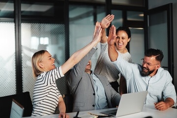 A group of people are smiling while holding their laptops.