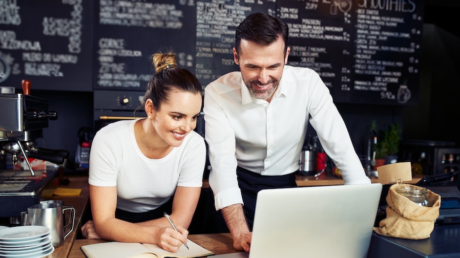 A picture of a male and female business partner pointing at a computer and discussing how to separate business and personal finances.