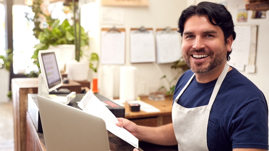 A smiling person in a white shirt and a laptop.