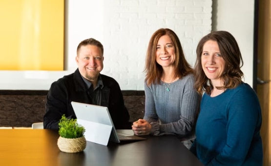 A photo of three people sitting at a table smiling.