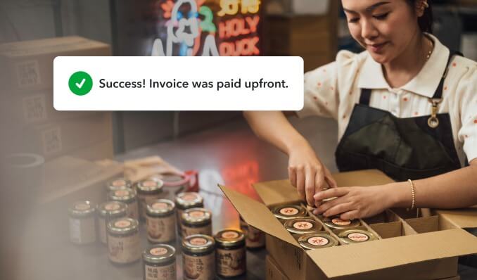 Business owner packs merchandise while getting a notification from QuickBooks that their invoice was paid in advance.