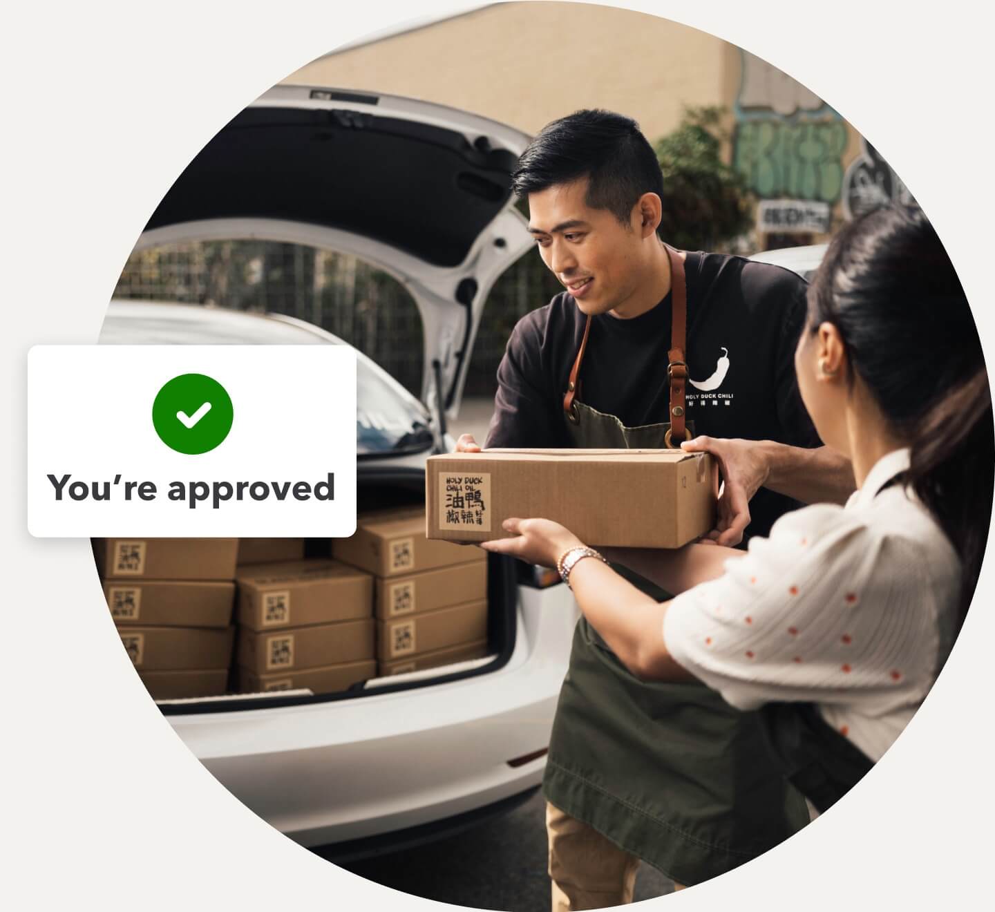 Business owner loads merchandise into a car while QuickBooks shows a notification for approved funding.
