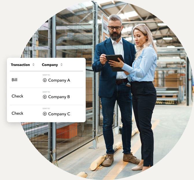 Man and woman standing in manufacturing warehouse looking at a tablet device discussing multi-company transactions