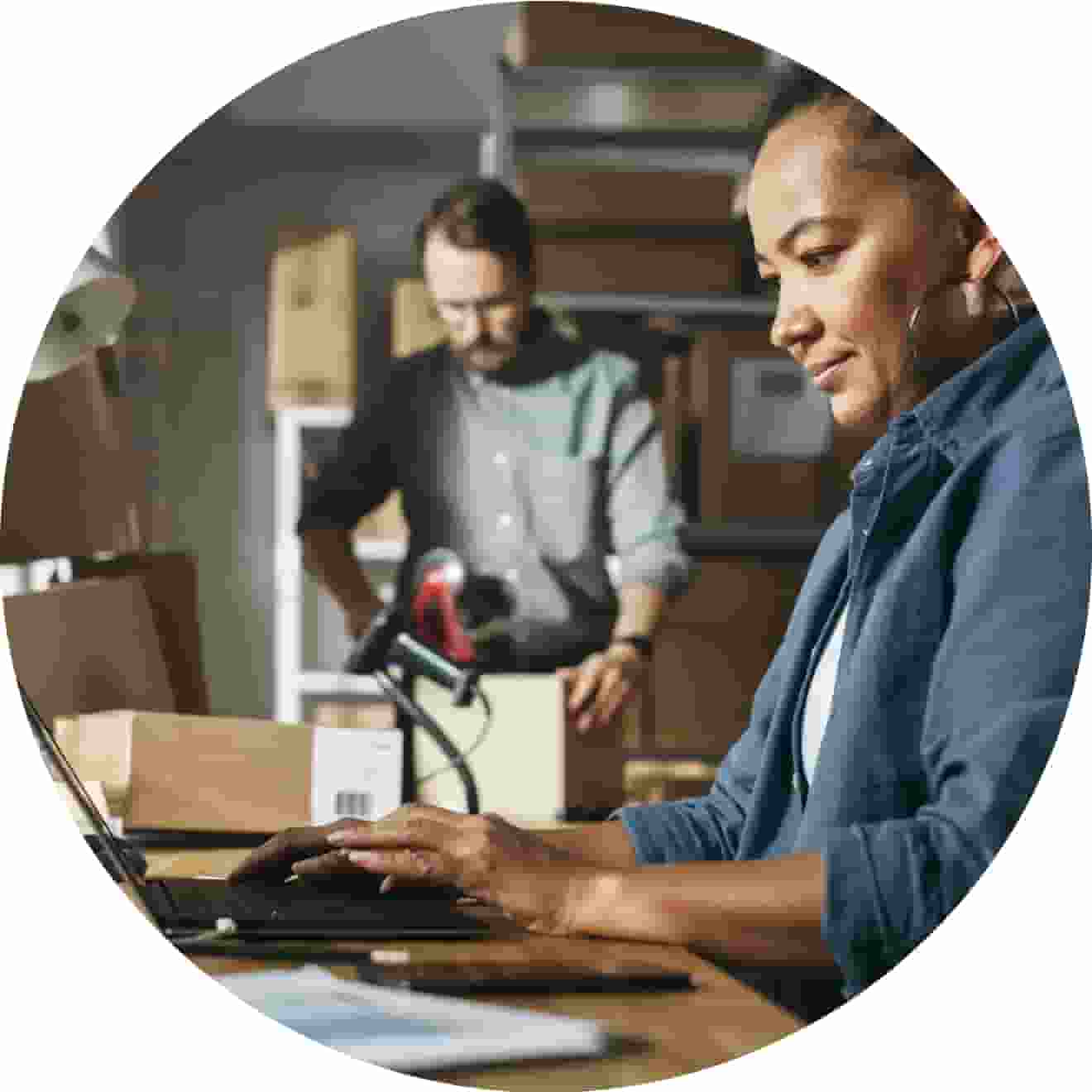 Woman on laptop with man in background doing product inventory