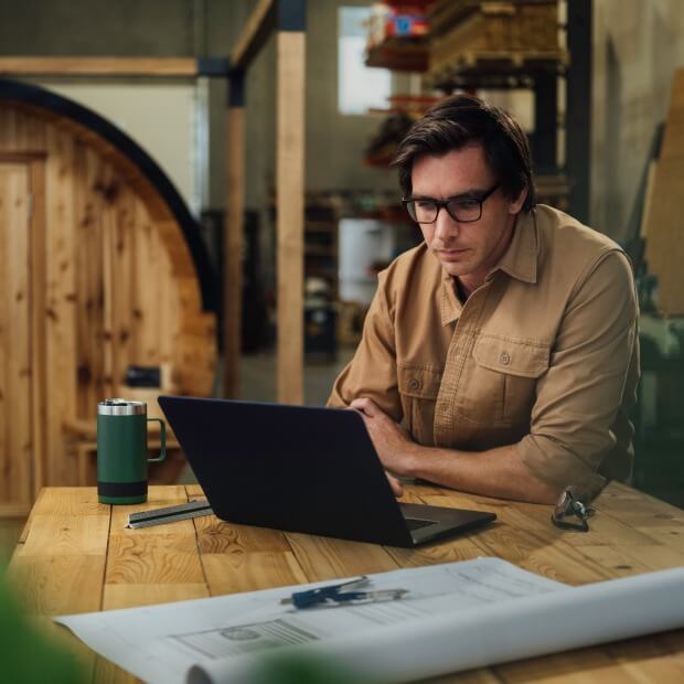 A business owner uses a laptop while sitting at a table reviewing business performance on QuickBooks Online Advanced.