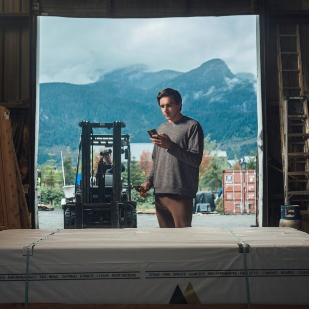 A manufacturing business owner works in the shop while using a mobile device.