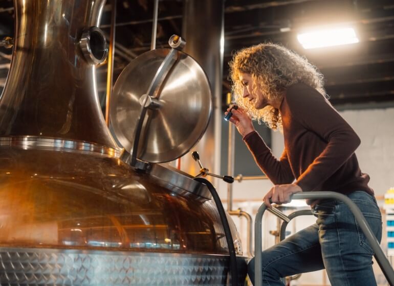 Small business owner inspecting a batch of artisanal gin in a large copper tank.