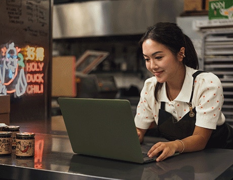 Small-business owner smiling while working on a laptop in a commercial kitchen.