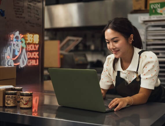 Small-business owner smiling while working on a laptop in a commercial kitchen.