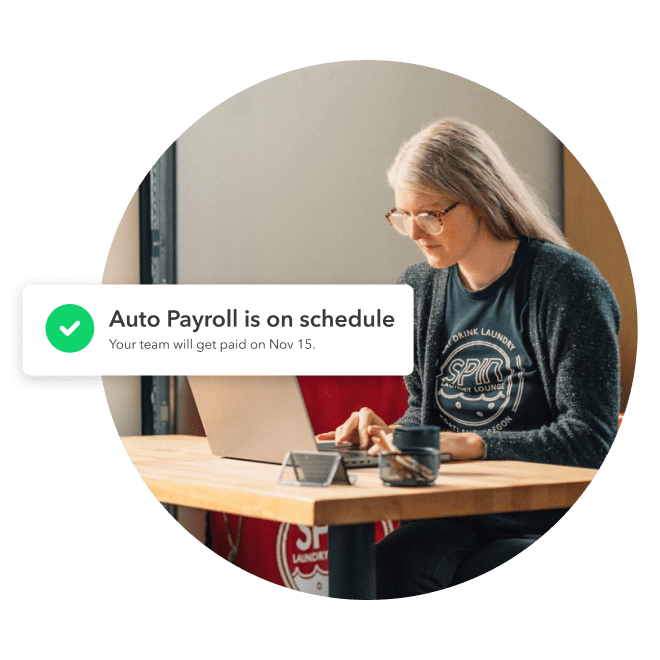 Female business owner sitting at desk with an auto payroll message indicating her team will get paid on Nov. 15.