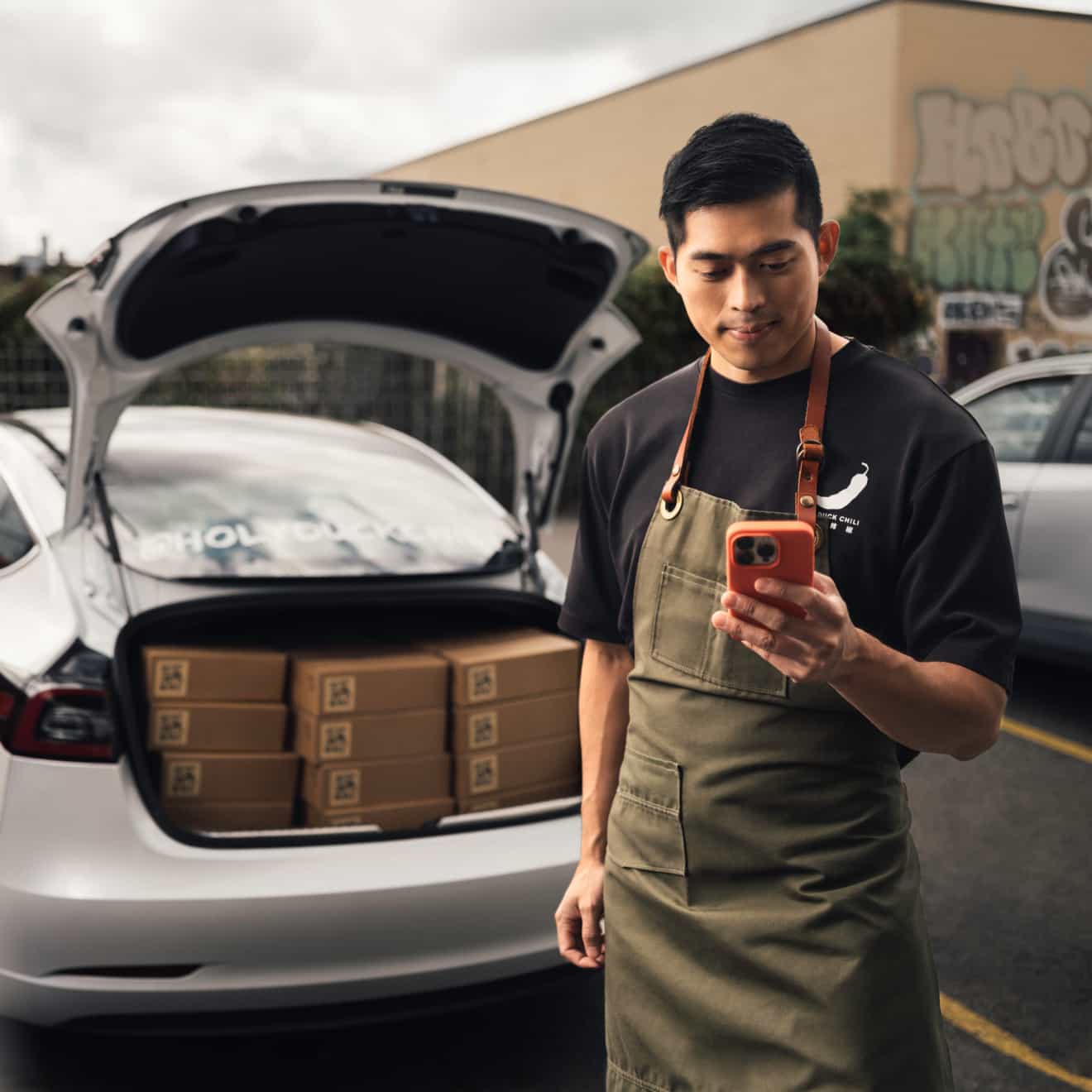 Small-business owner using a phone to keep track of time, with orders prepared for delivery in a car trunk.