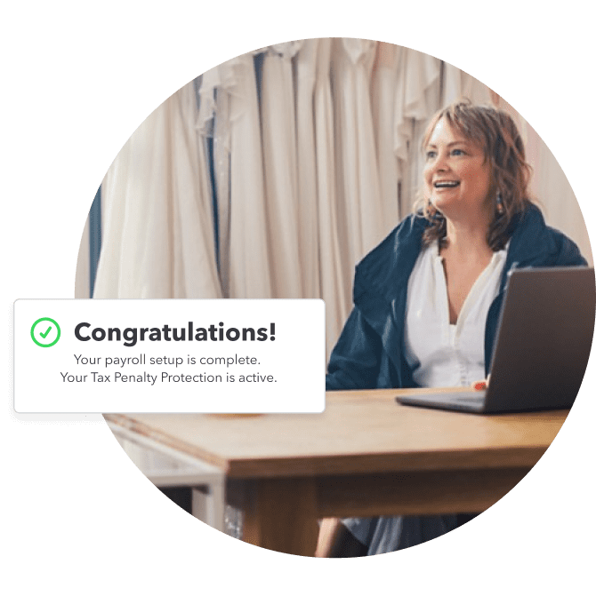 Woman sitting at a desk with an open laptop and an overlay image with congratulations message saying, your payroll setup is complete. Your tax penalty protection is active".