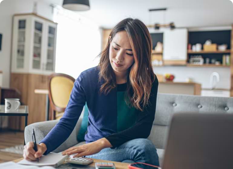 A person in a living room is sitting at a coffee table writing in a notebook.