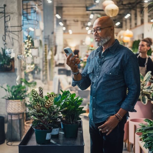 A business owner of a plant nursery is holding a mobile phone. 