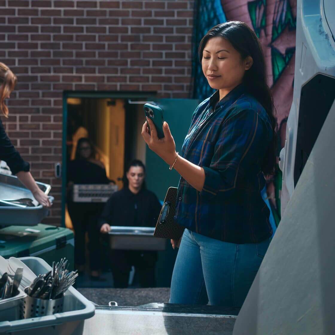 Person on a phone overseeing food trays getting loaded in a van for a catering event and snapshot of quick actions.