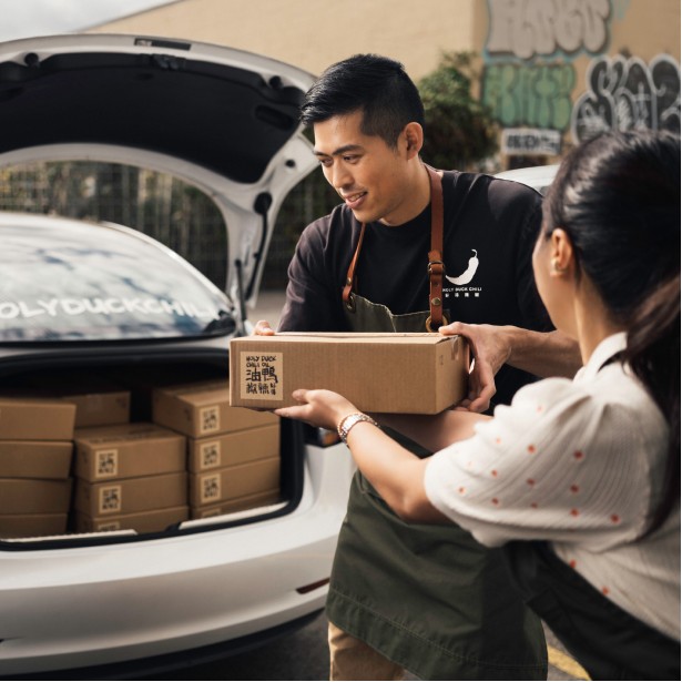 A business owner loads boxes of bottled foods into a car for delivery.