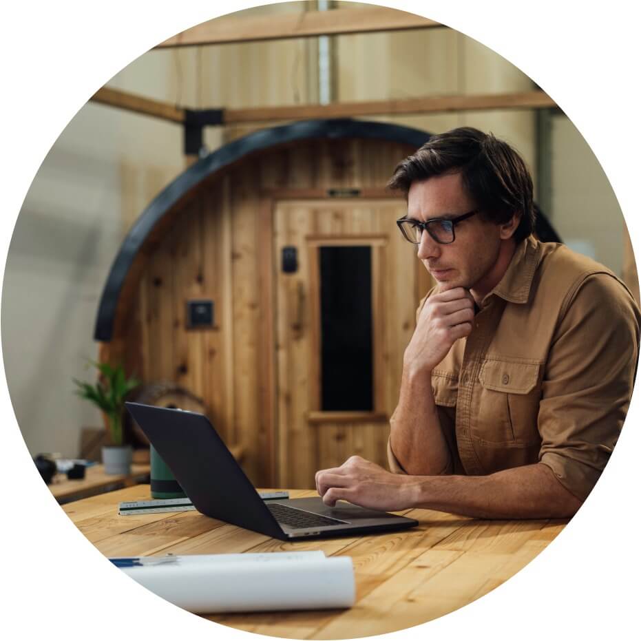 Businessman sitting at a table inside a warehouse working with an open laptop.