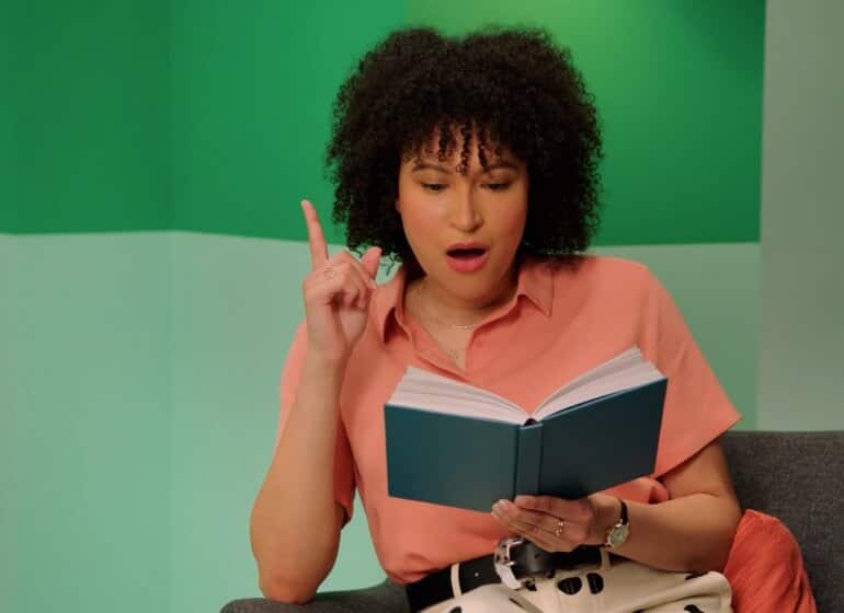 A photo of a person reading a book and lifting their pointer finger up as if they have a good idea.