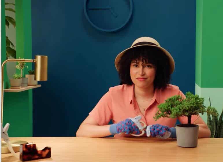 Photo of a person sitting at their desk with gardening gloves on and a potted plant placed in front of them.