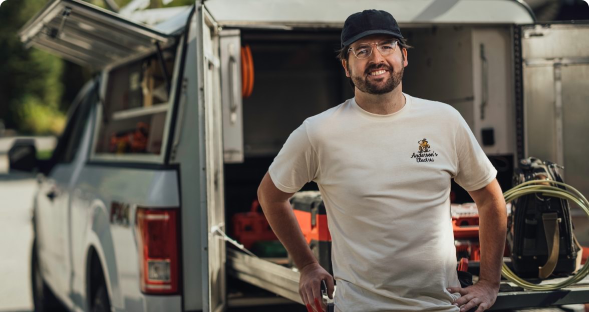 Electrician smiling after a job well-done, while leaning against a work truck.