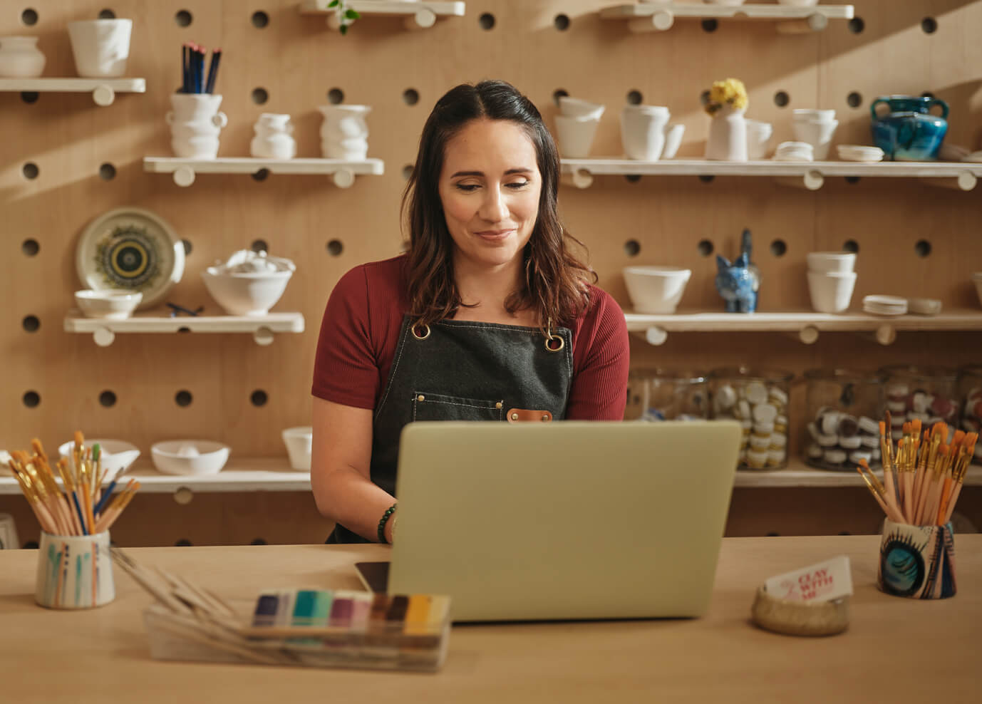 Person working on a laptop in a pottery studio .