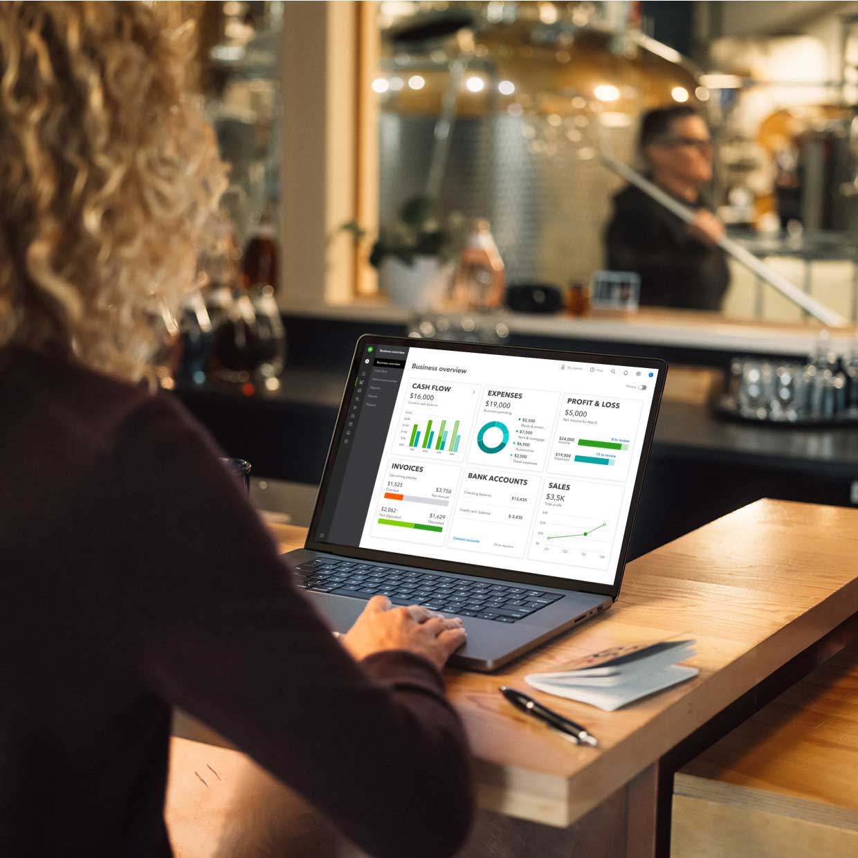 A brewery owner sits at a table in the restaurant with a laptop open to the business performance data in QuickBooks Online.