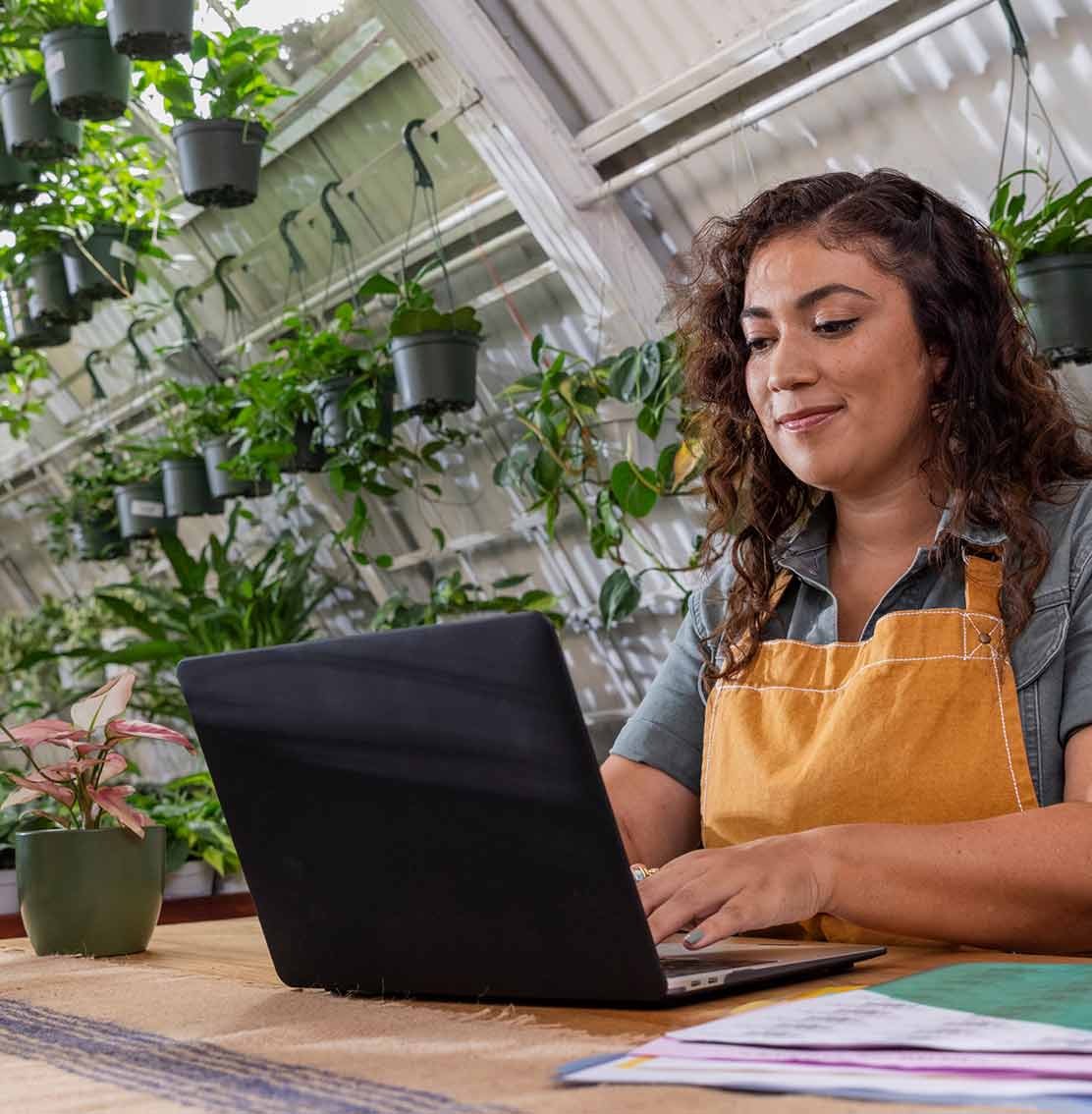 Owner of a plant store sitting in front of a laptop at a table reviewing  business transactions in QuickBooks. 