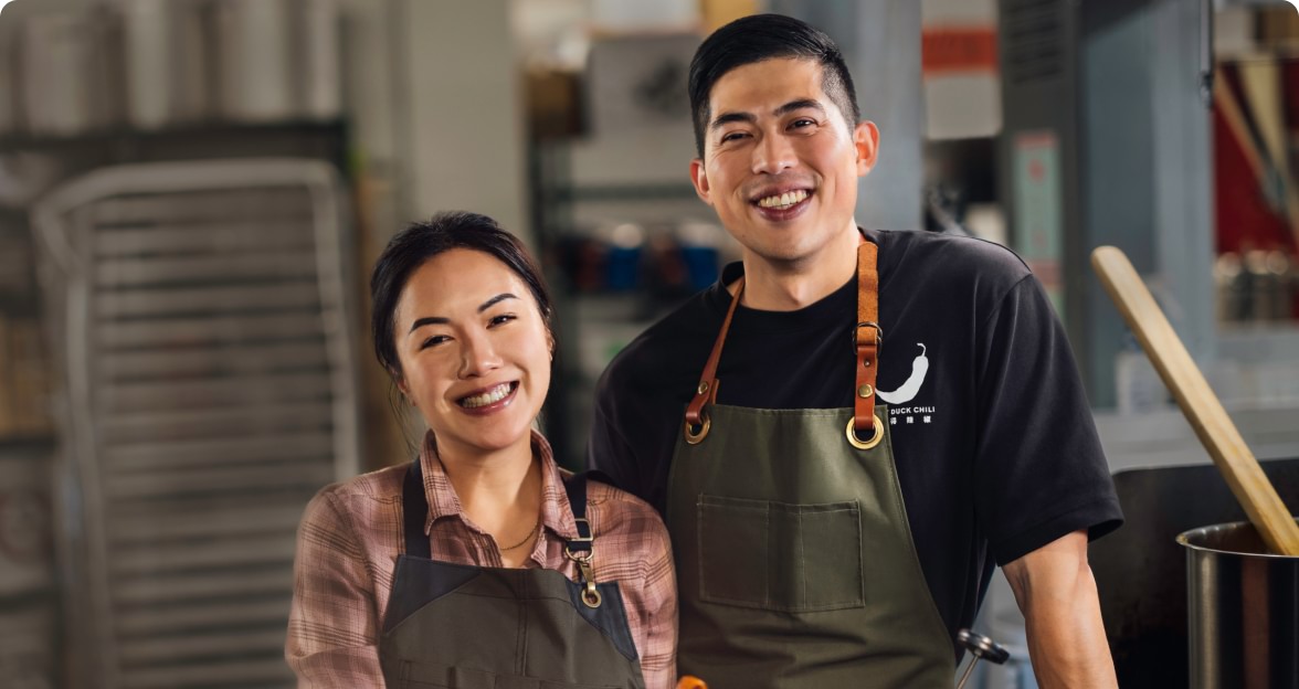 Two small-business owners smiling proudly in their kitchen.