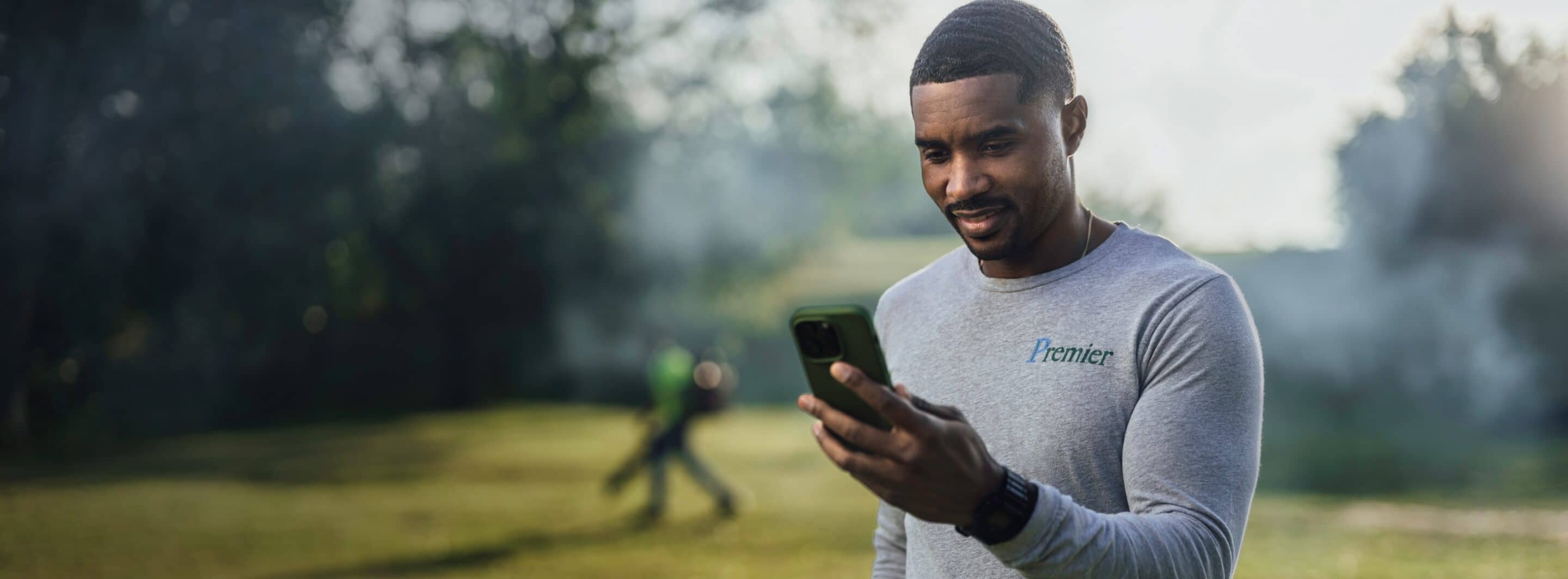 A business owner at a landscaping job holding a phone and looking down at the screen.