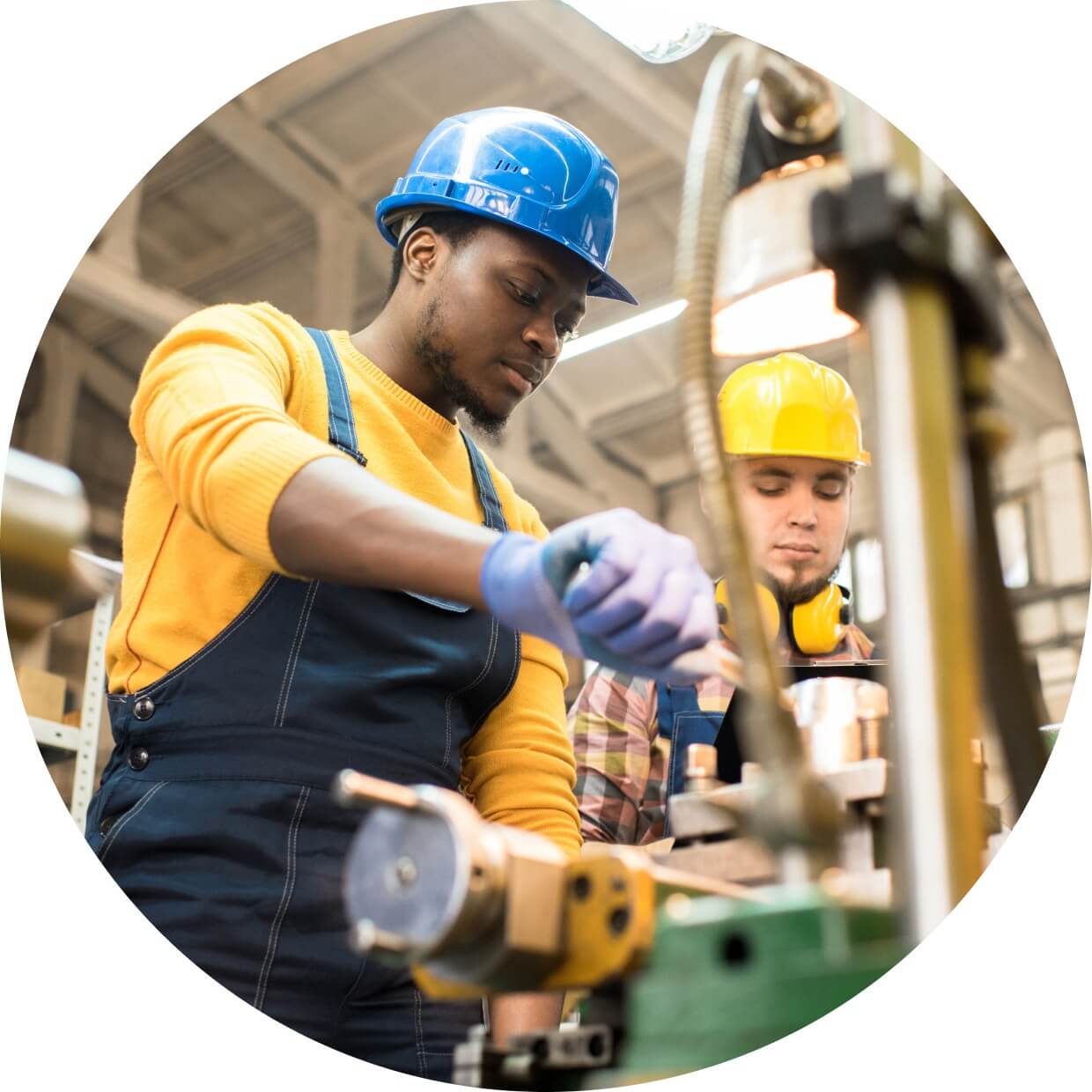 Two manufacturing workers wearing hardhats and operating machinery in a factory. 