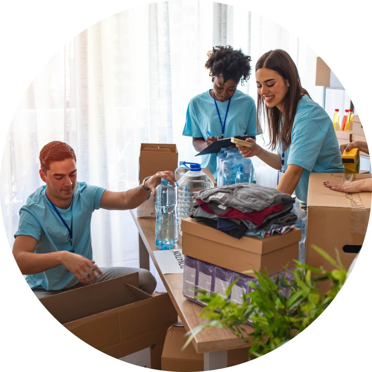 A group of three nonprofit workers organizing water, clothing, and other boxed supplies at a donation table.