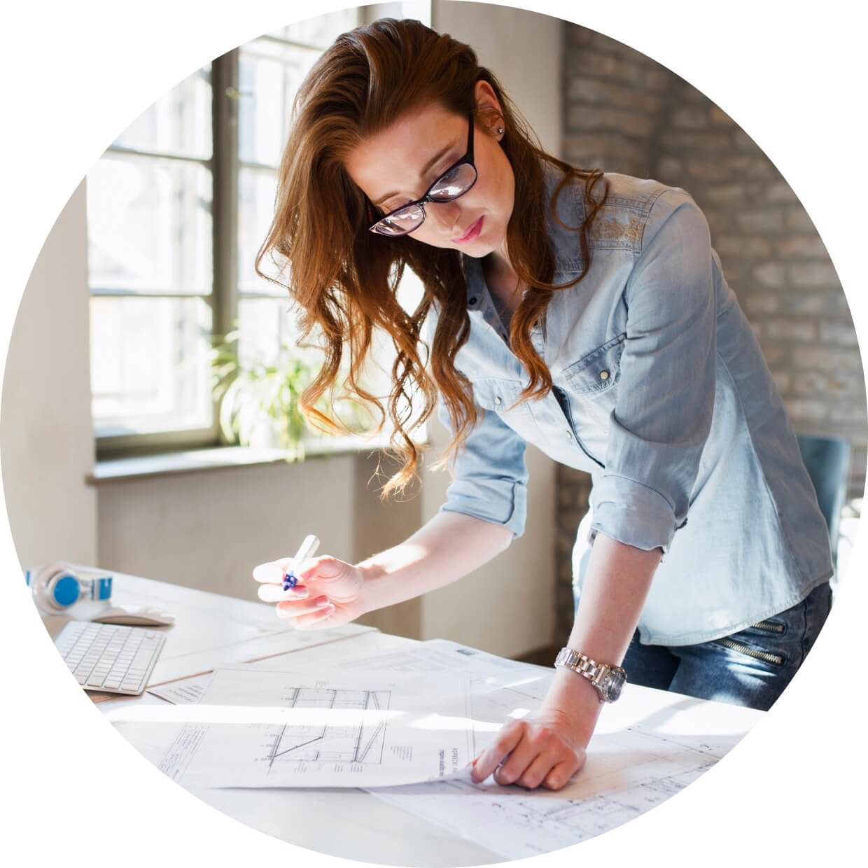 A business owner standing in her office drafting plans on papers strewn across a table.