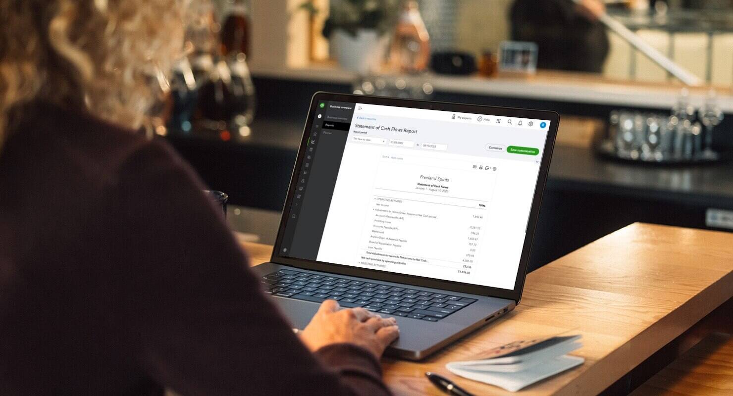 Woman using QuickBooks to run a cash flow statement on laptop. 