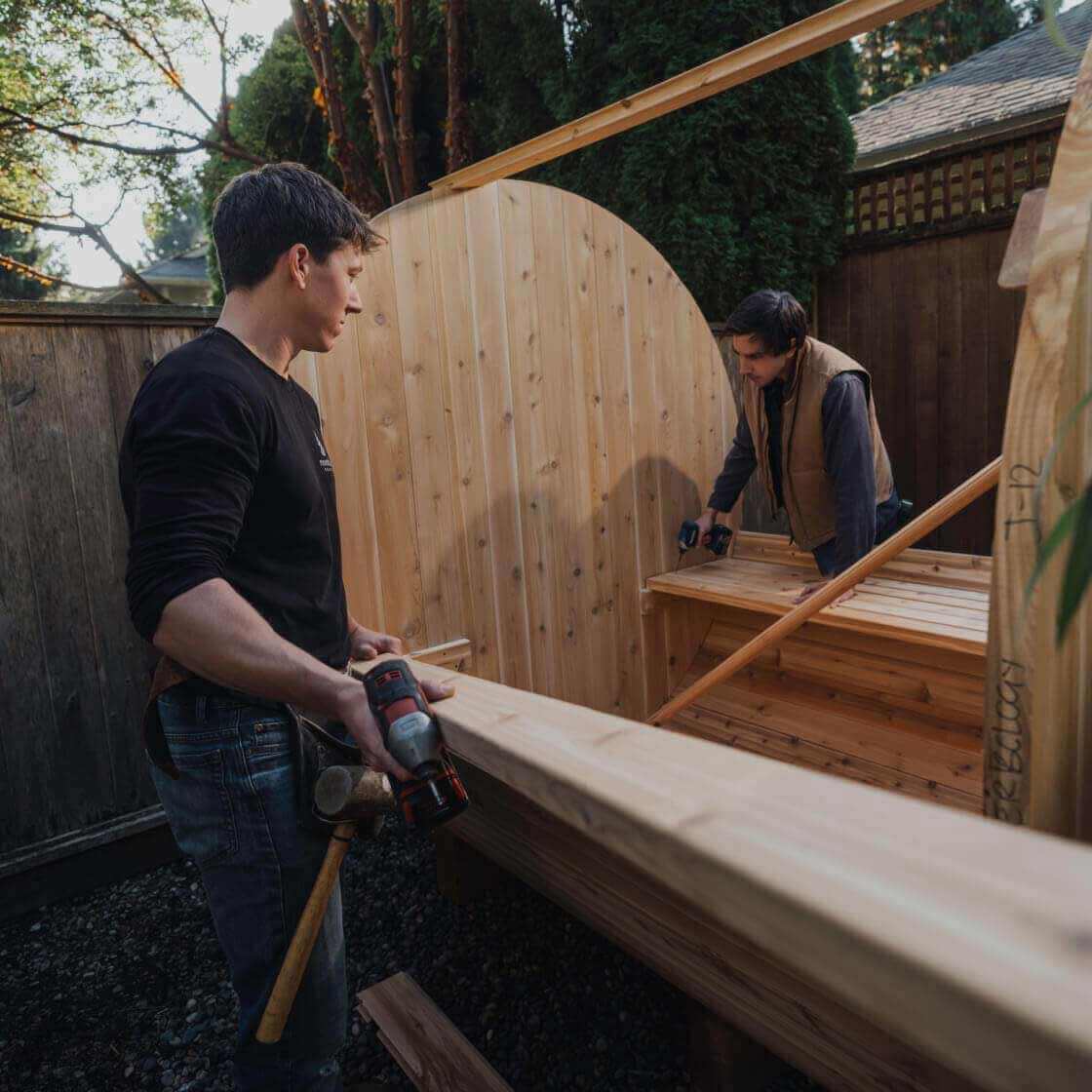 Two persons installing a sauna in a backyard, and using power tools