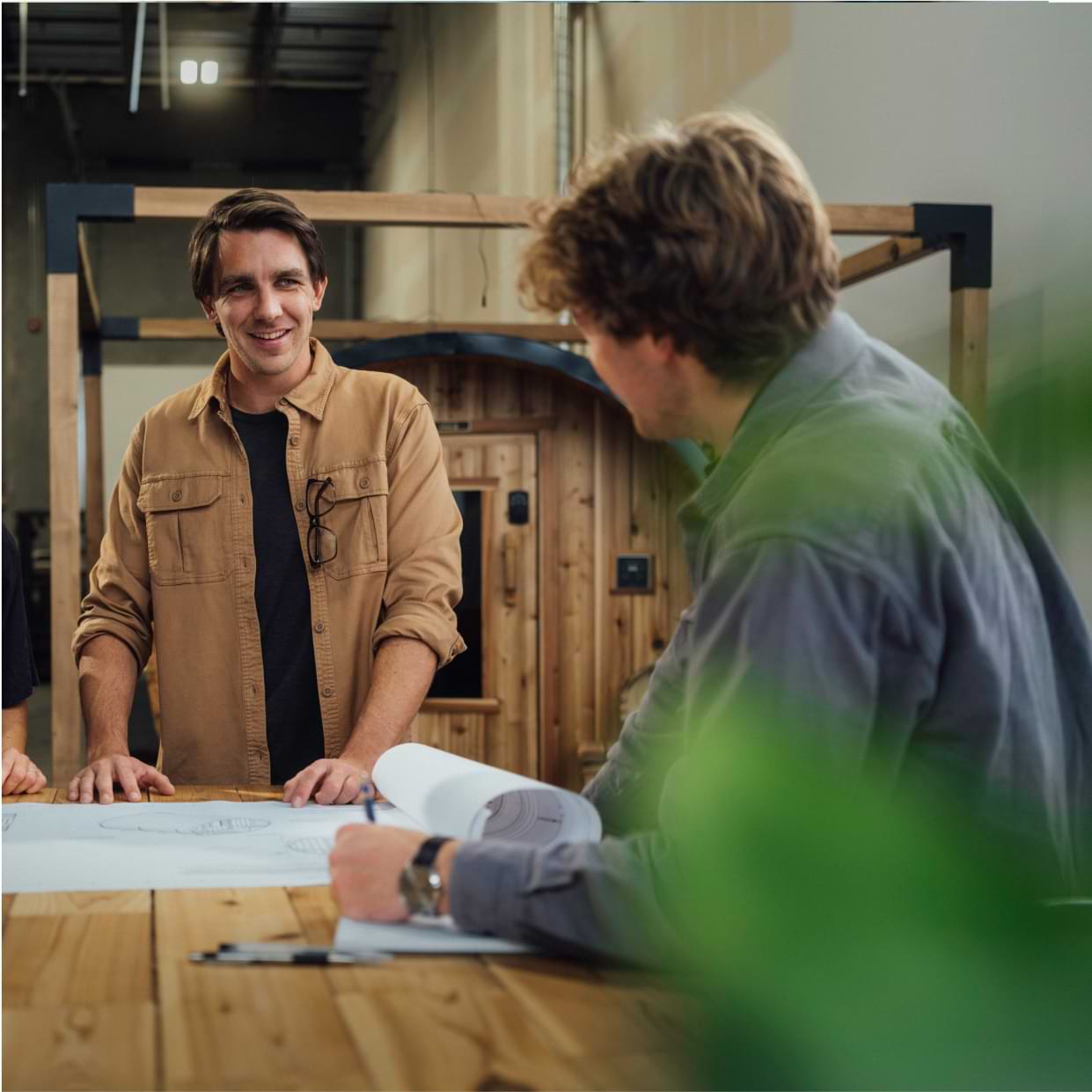 Business owner talking with employees over building plans in a manufacturing warehouse.