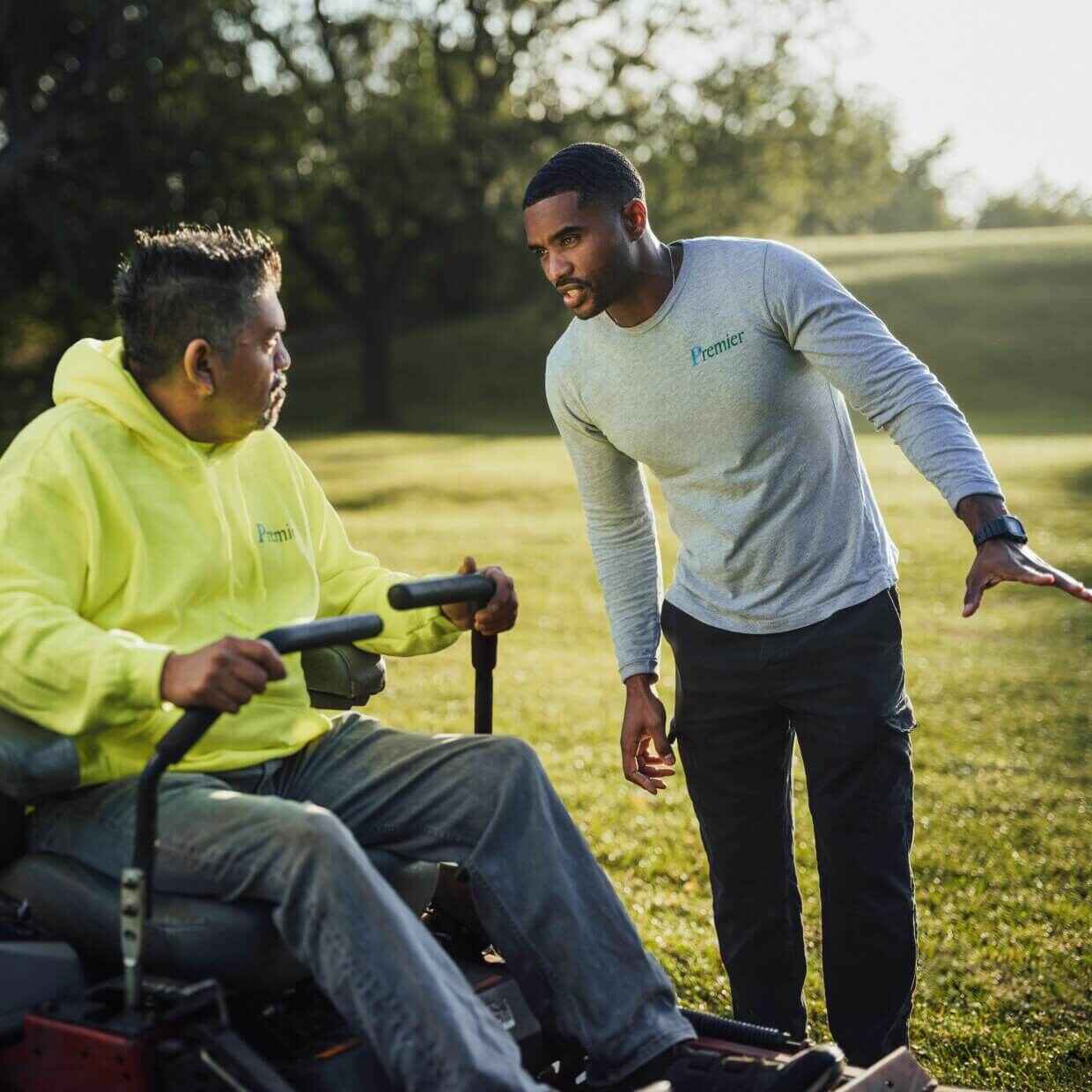 Landscaper directing an employee driving a lawn mower on-site at a field.