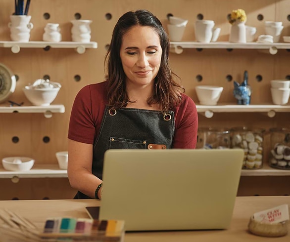 Woman working on laptop in pottery studio workspace