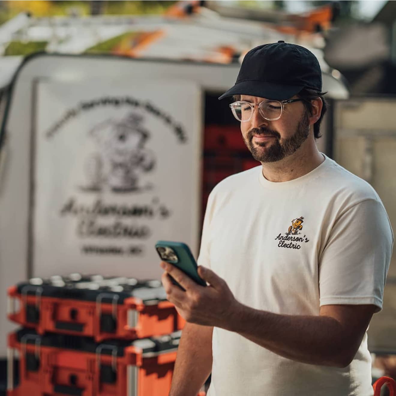 An electric company contractor standing in front of an equipment trailer looking at his mobile phone.
