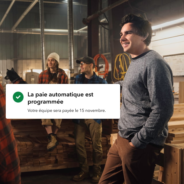 Le propriétaire d'une petite entreprise avec des employés sourit en discutant dans un atelier. Un message contextuel indique « La paie automatique est dans les délais ».