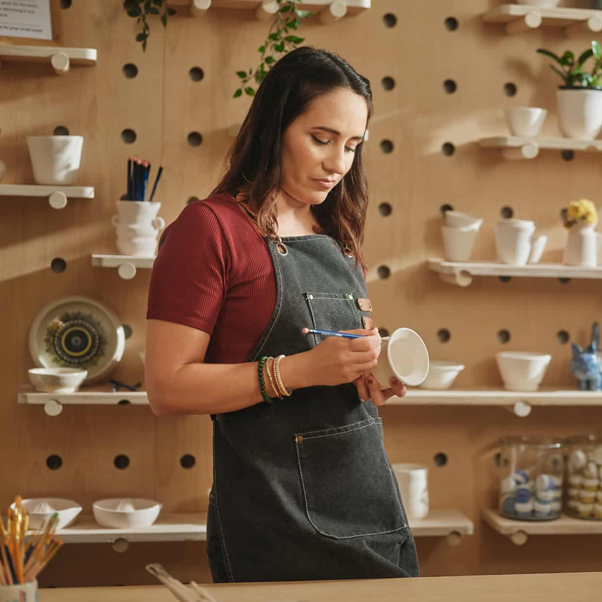 Une femme dans son atelier peint sur une tasse en argile.