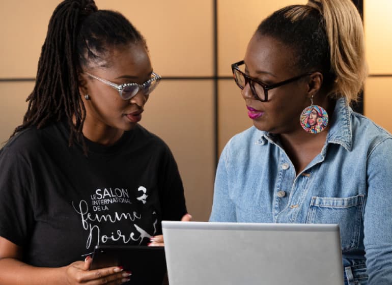 Two stylish women consult over a laptop.