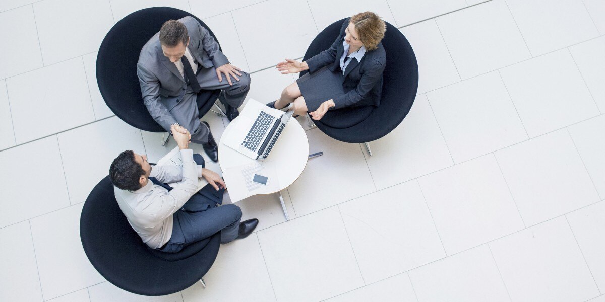 imagem aérea de três pessoas sentadas em poltronas redondas e na cor azul com uma mesa branca com um notebook ilustrando artigo sobre o que é contabilidade societária