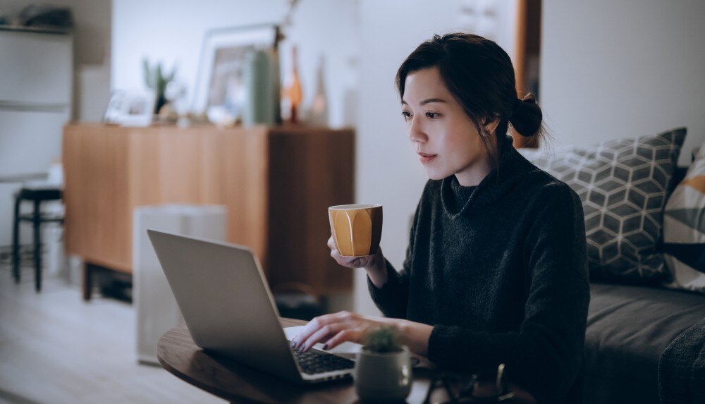 imagem de uma mulher segurando uma xícara de café e olhando para um notebook enquanto trabalha em casa ilustrando artigo sobre como calcular honorários contábeis